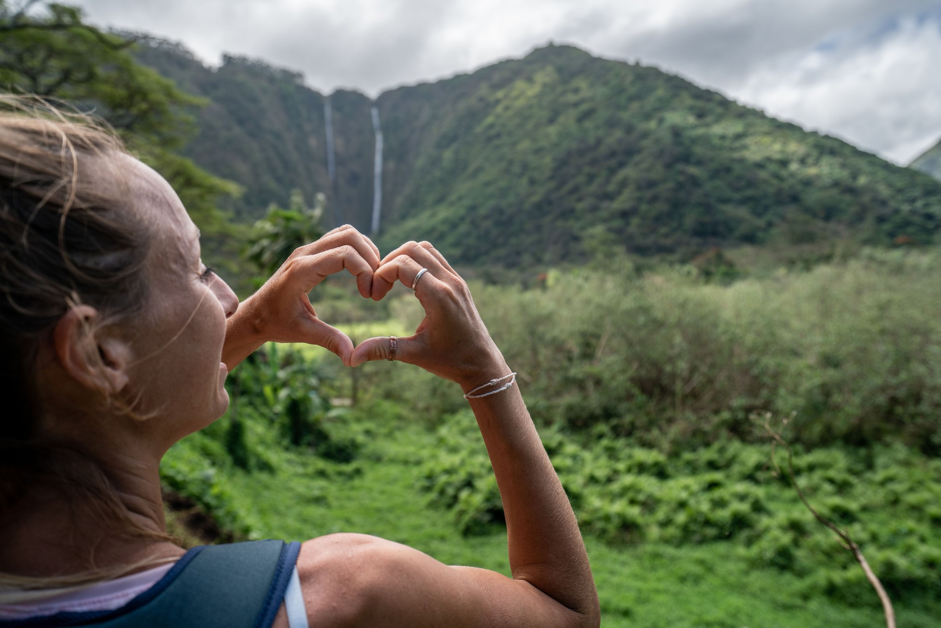 Hiking woman making heart shape with hands on Waipio valley, Hawaii